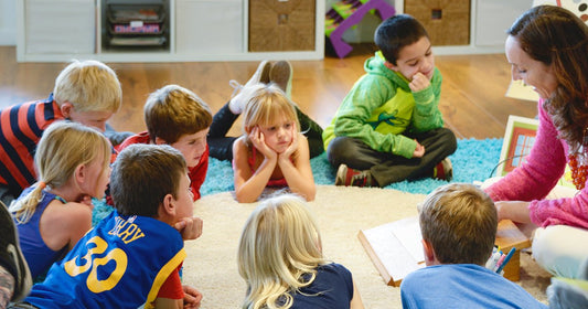 A teacher showing picture cards to a group of children sitting on the classroom rug